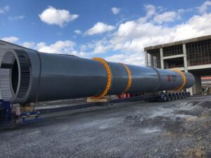Large industrial rotary drum being transported on a multi-axle trailer at a construction site