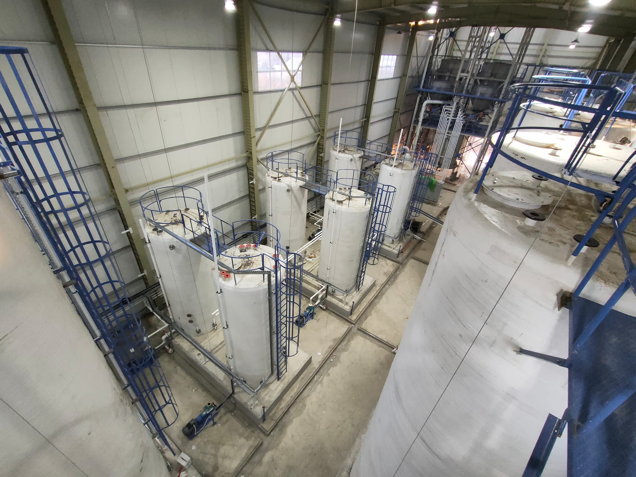 Elevated view of large white industrial storage tanks inside a manufacturing facility