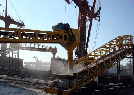 Conveyor and hopper system operating at an industrial port with cranes in the background