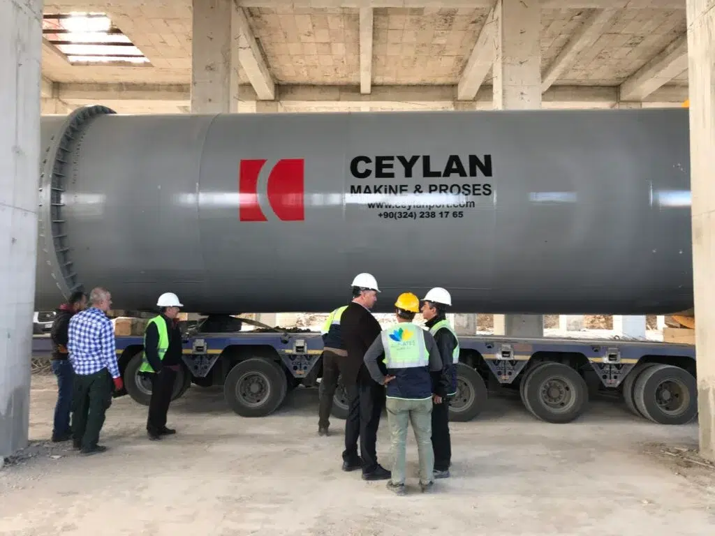 Large industrial rotary drum on a trailer with workers standing beside it inside a building